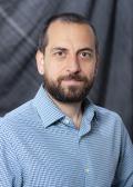 A portrait of a man with brown hair and brown beard, wearing a blue button down shirt 