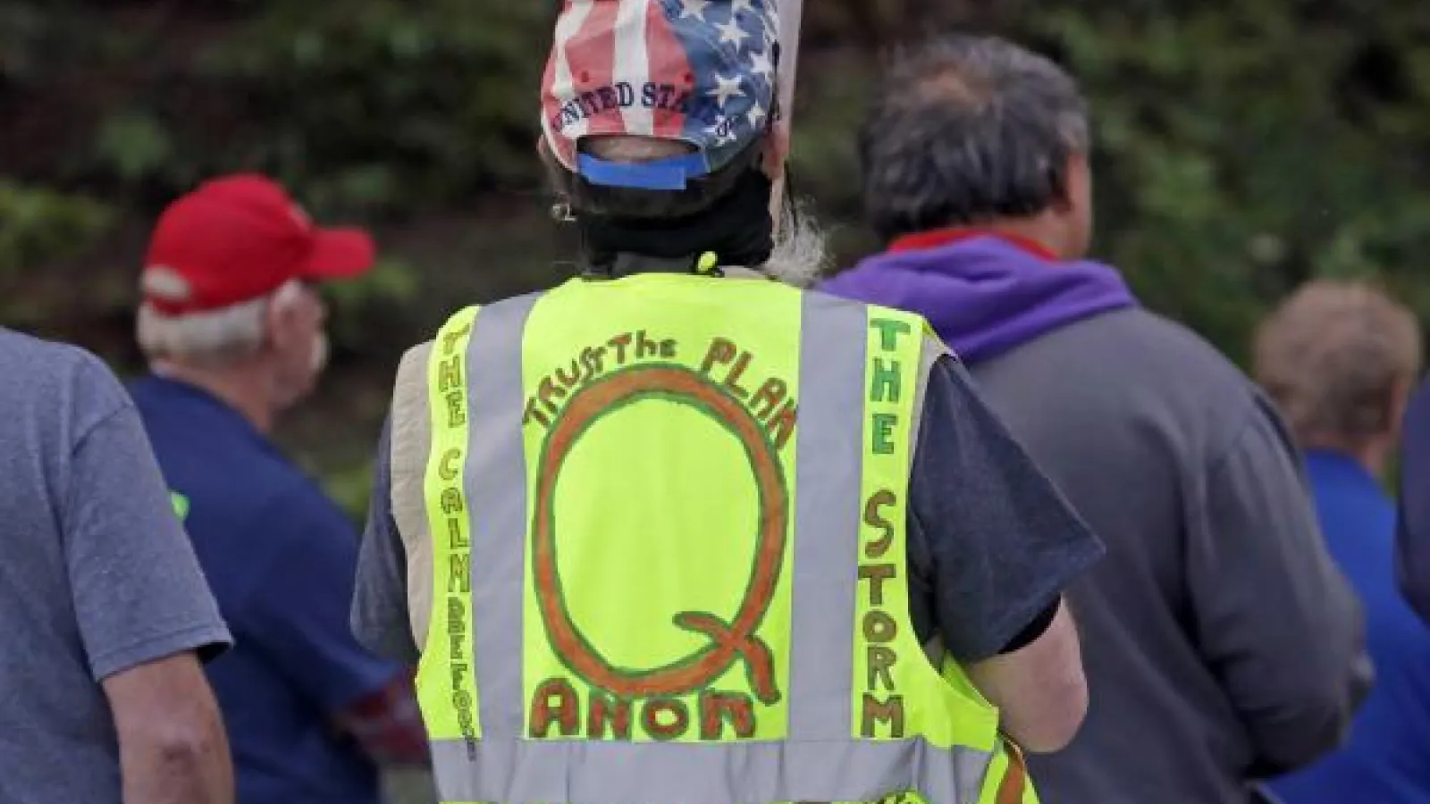 A man with a neon vest that says Q Anon