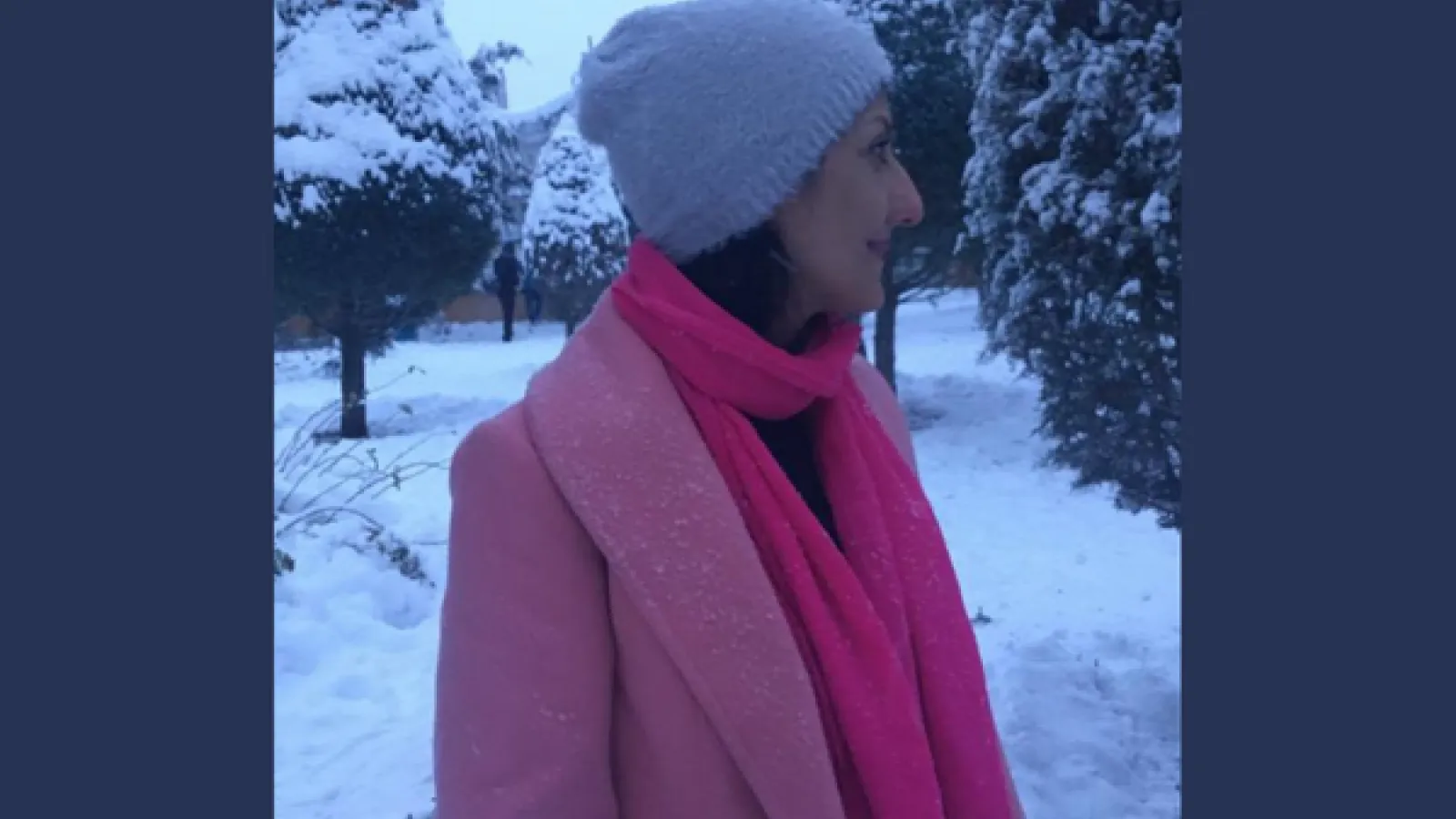 Portrait of a woman wearing a pink coat and pink scarf against a snowy background with trees