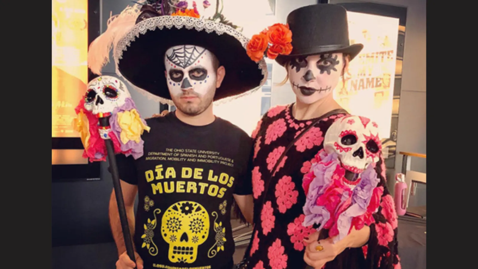 A man has a skull painted on her face and a woman is wearing a top hat with a skull painted on her face