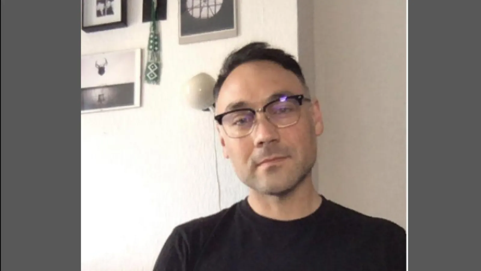A man with a black crew neck shirt and 1950s style glasses