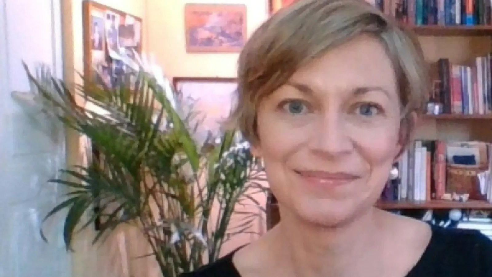 A front facing portrait of a white woman with short blonde hair in front of a bookcase