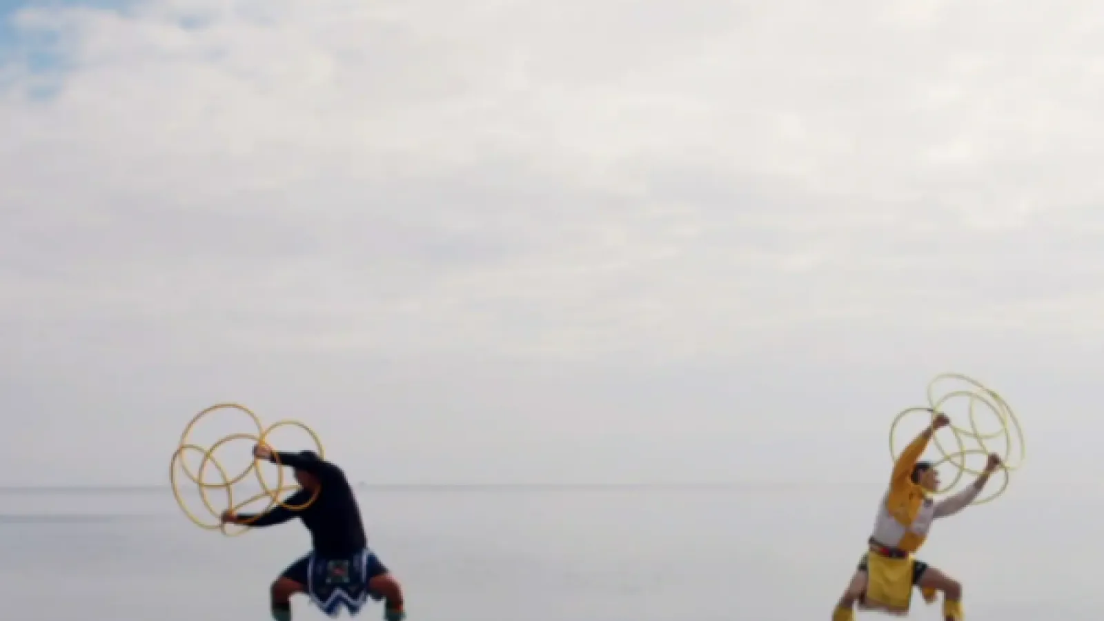 Two people on a beach with a big sky holding hula hoops