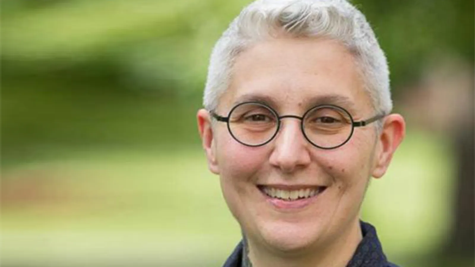 Woman with short grey hair and round glasses smiling at camera