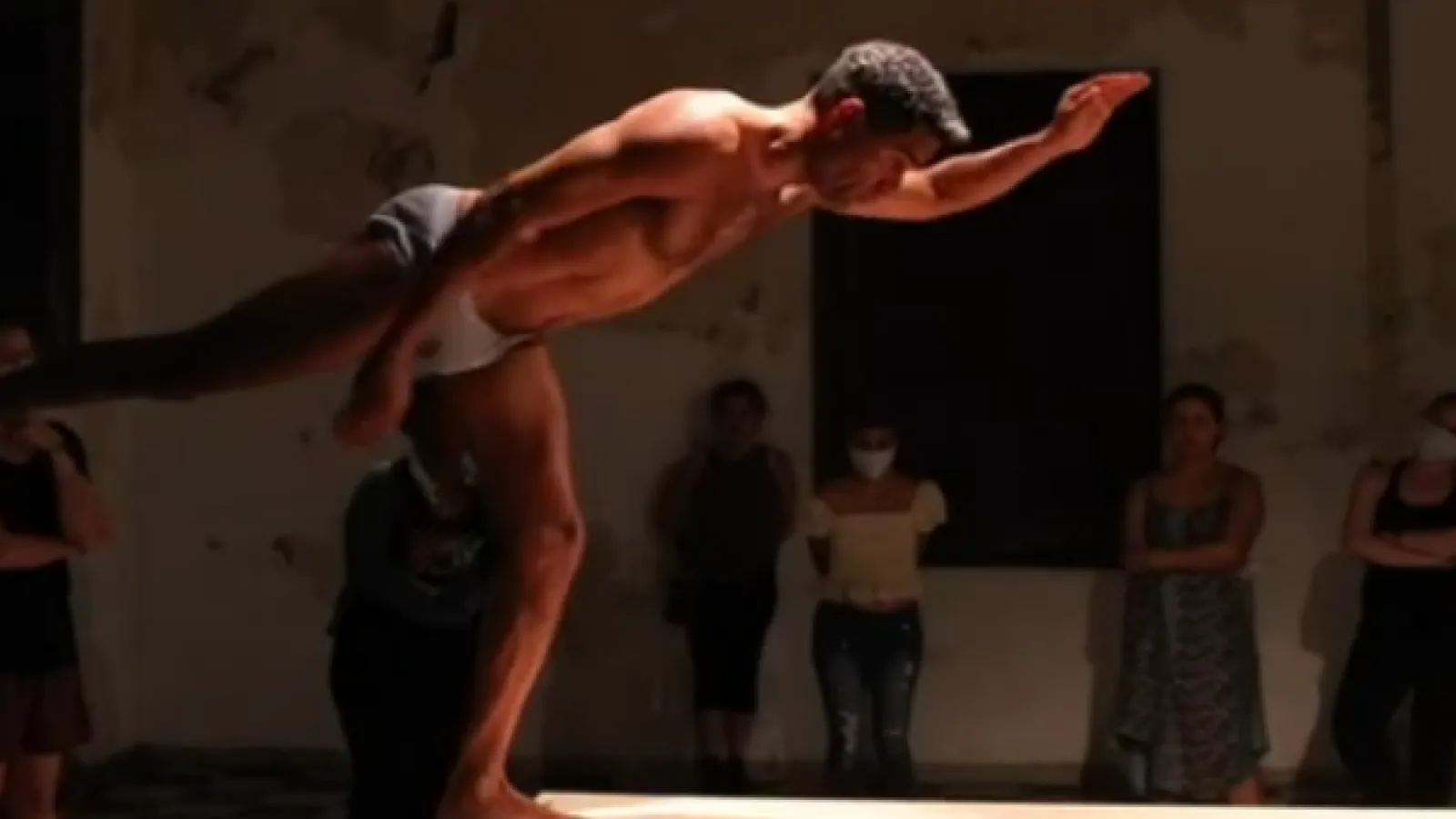 A nearly naked man balances on the edge of a table outstretching his arms and legs. 