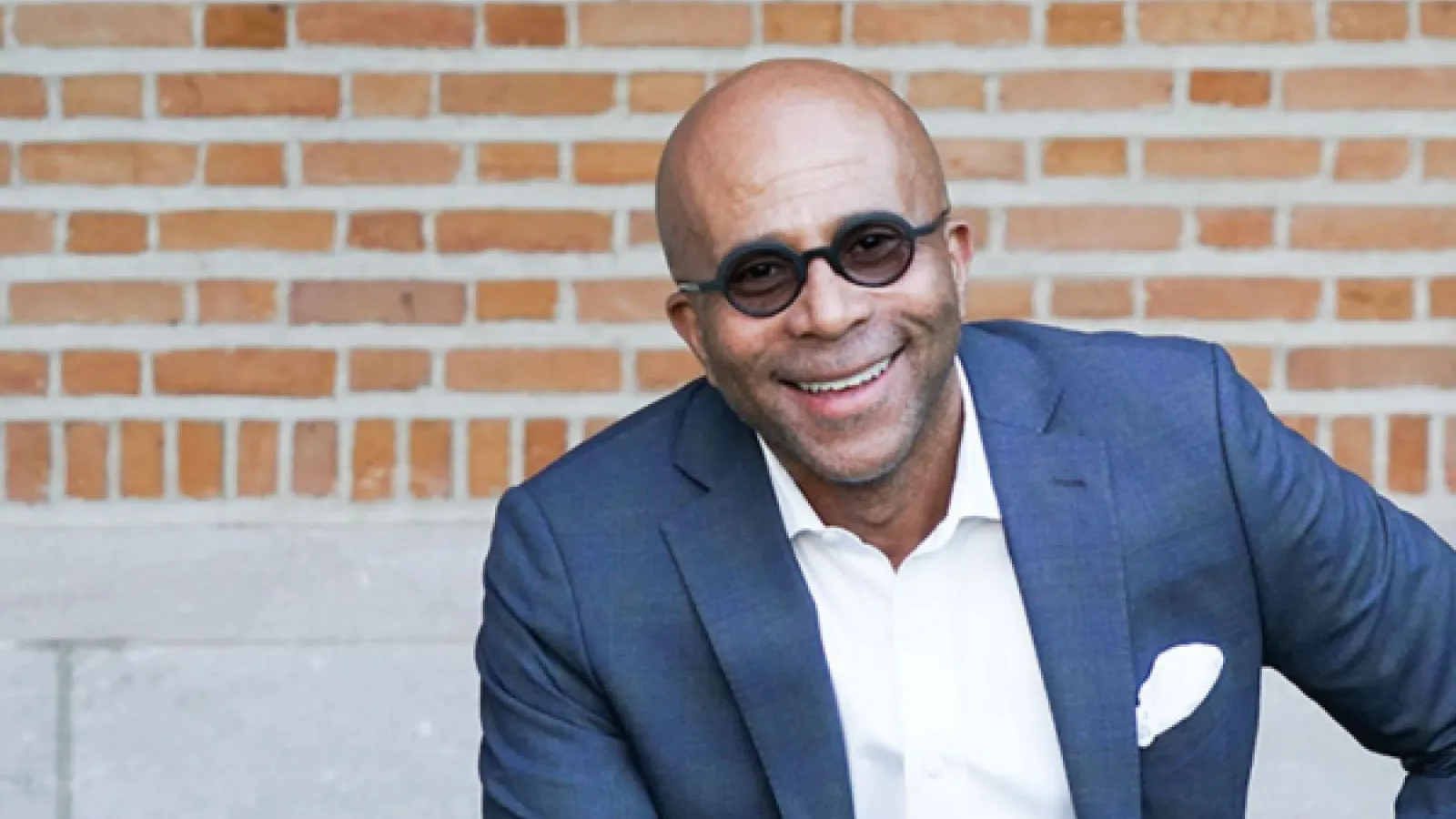 Man with sunglasses and in a suit smiling at camera