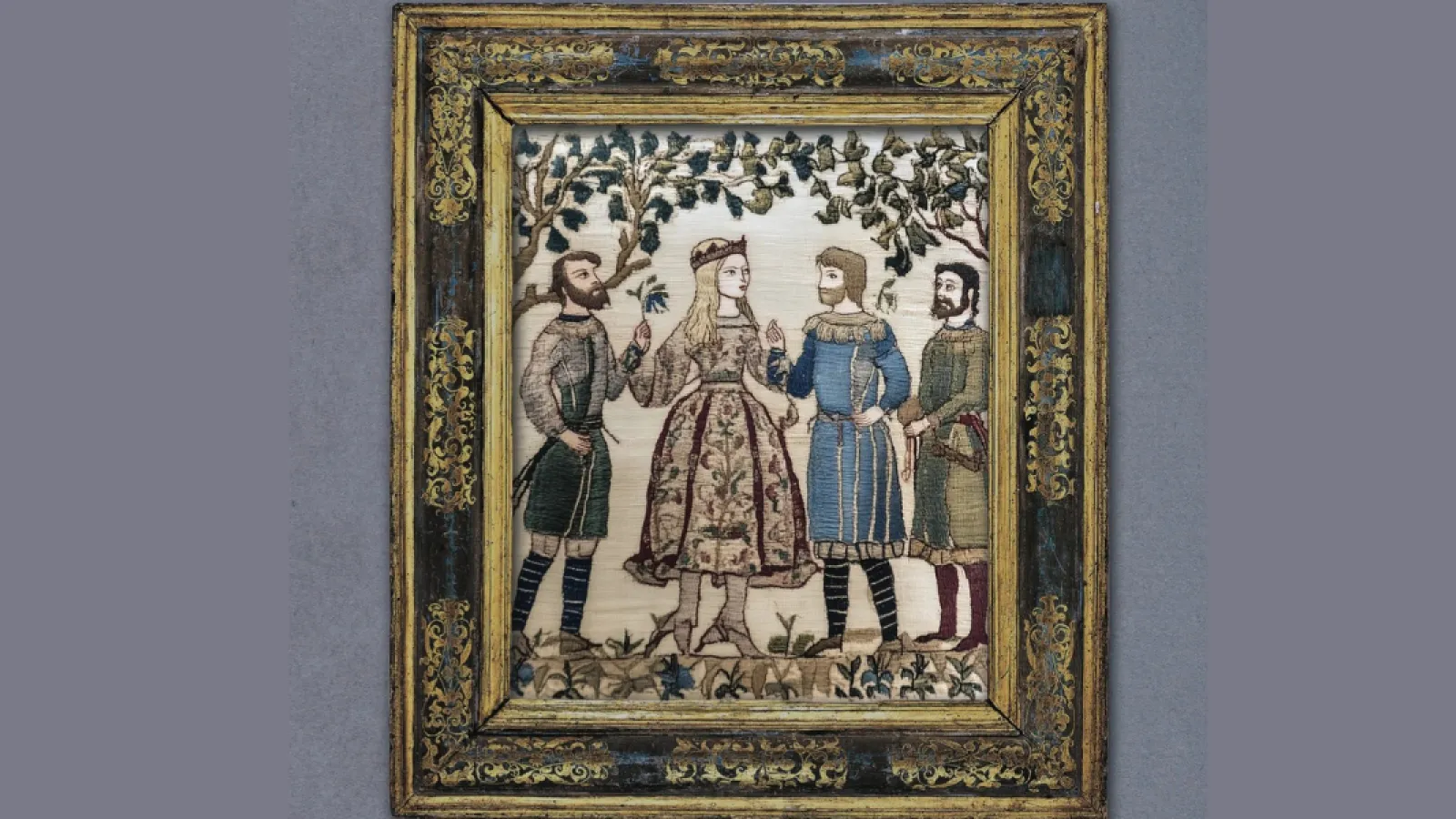 An embroidered scene with a young woman in the middle and two men on either side. They are wearing medieval clothing. 