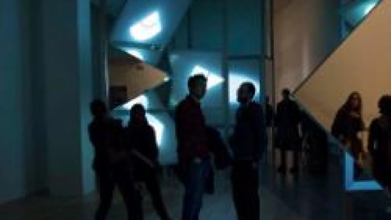 People in a dark room standing before four beams of light