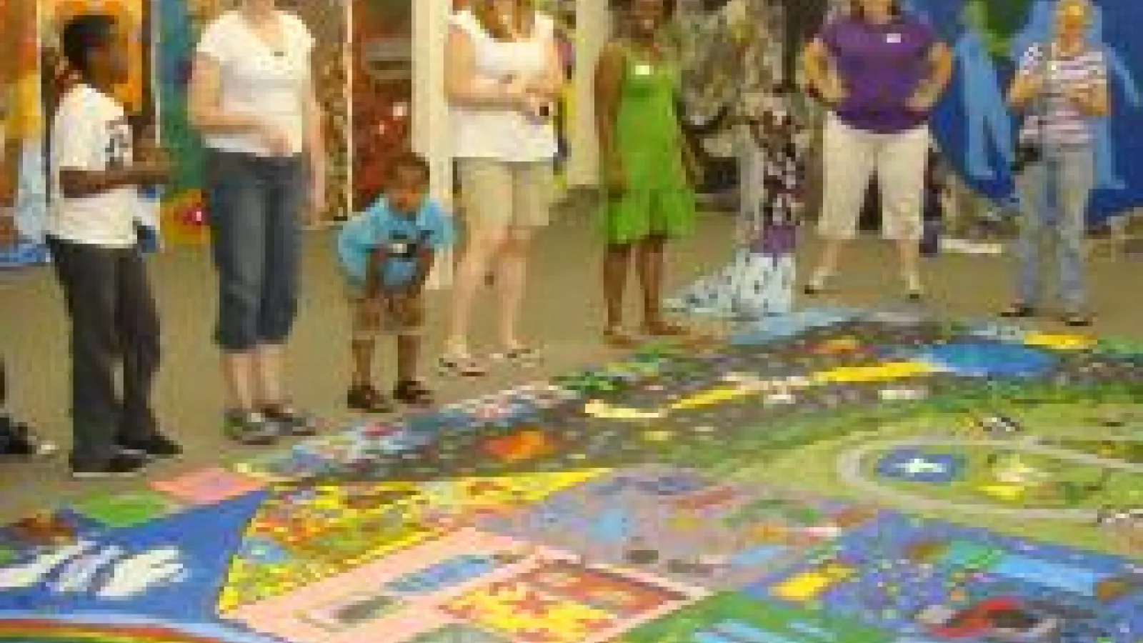 Children standing around a colorful mural that is painted on the floor