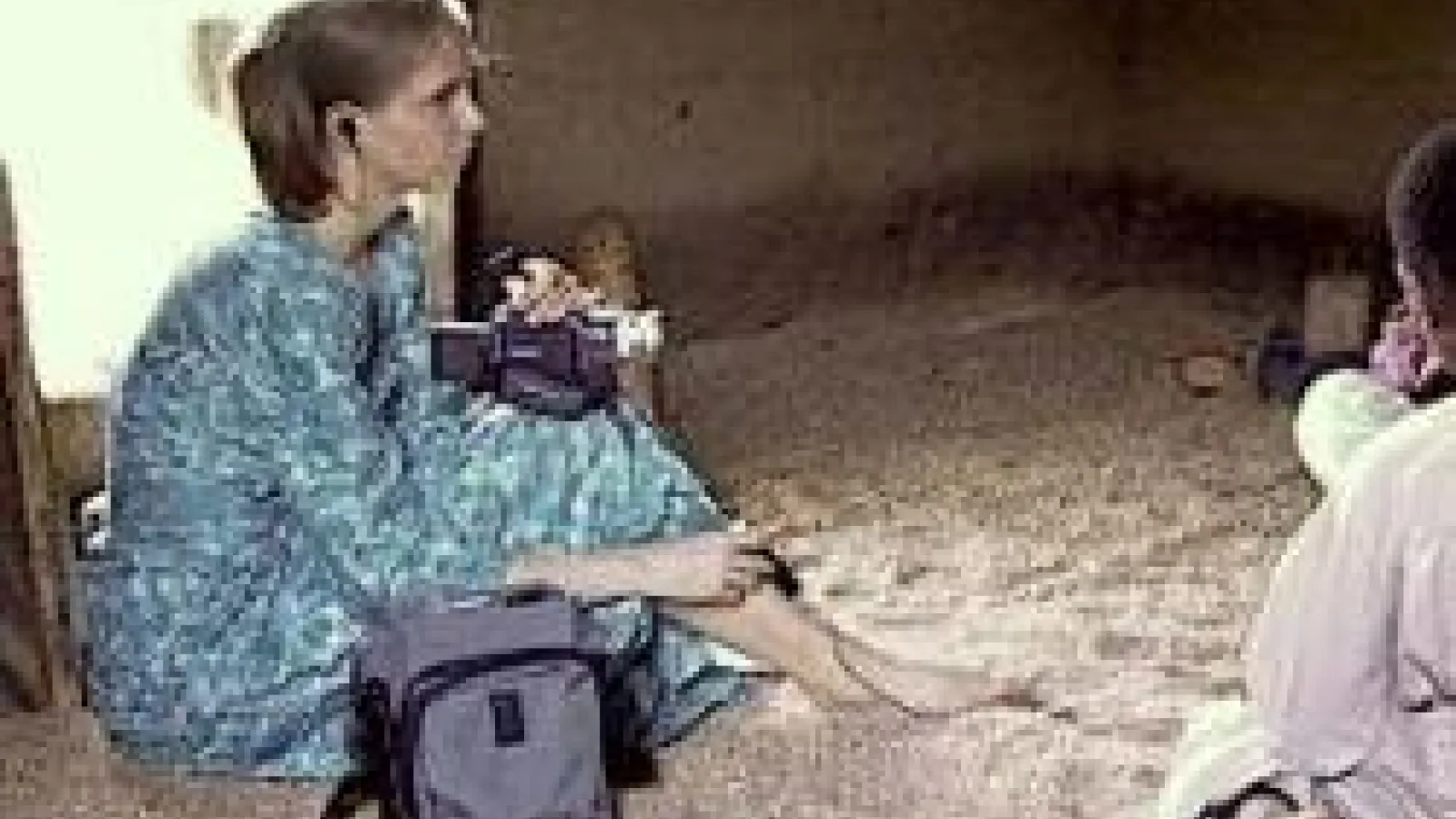 A young woman sitting on a dirt floor holding a video camera