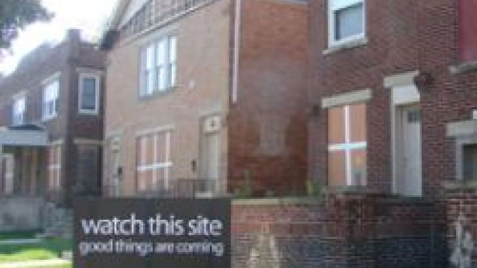 Two brick buildings with a sign that reads watch this site good things are coming