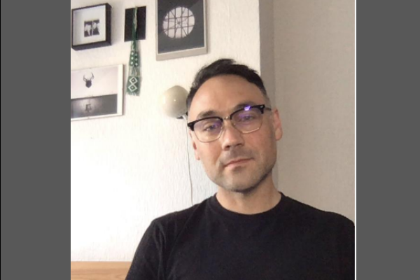A man with a black crew neck shirt and 1950s style glasses