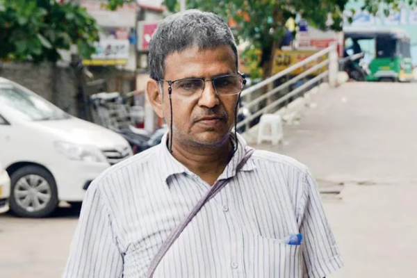 A man with grey and black hair, in the background is a road and a white car