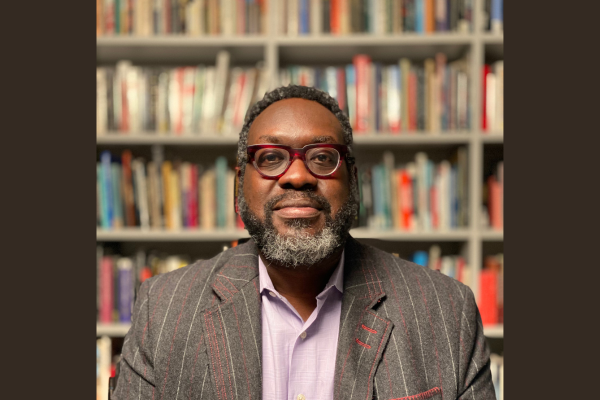 Image of Michael B. Gillespie in front of a bookcase. Michael is wearing a pink shirt with a blazer.