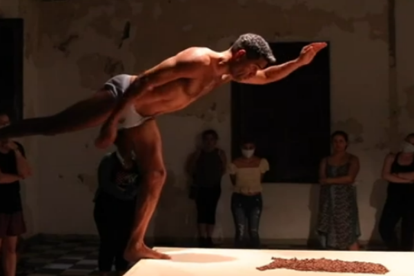 A nearly naked man balances on the edge of a table outstretching his arms and legs. 
