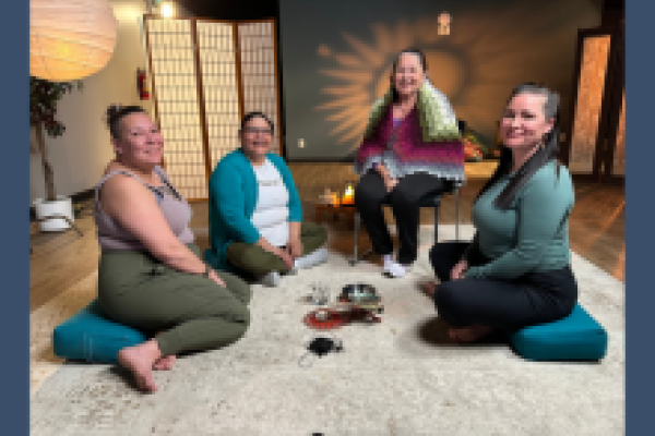 Four women sit on the floor smiling at the camera