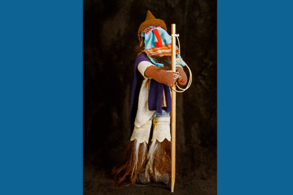 A cloth figure wears a mask and stands on legs made of feathers