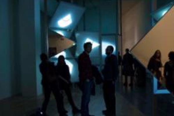 People in a dark room standing before four beams of light projected into the far wall