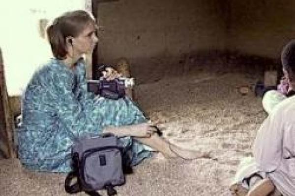 A young woman sitting on a dirt floor holding a video camera