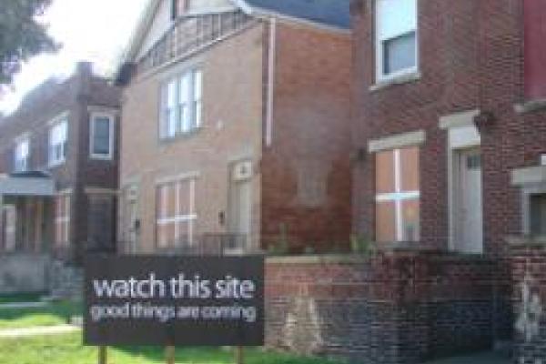 Two brick buildings with a sign that reads watch this site good things are coming