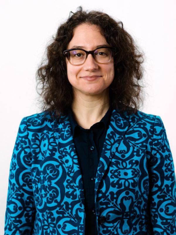 front facing portrait of a woman with black curly hair and black glasses. 