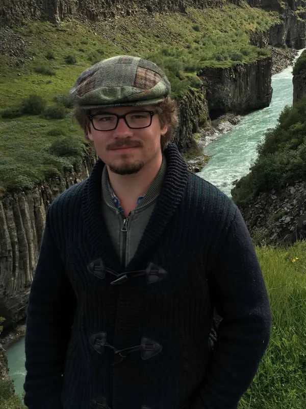 Liam Waters looking at the camera in front of a green landscape with a river running through it.