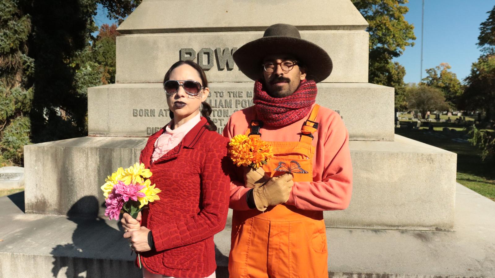 A man and a woman in costume in front of a gravestone